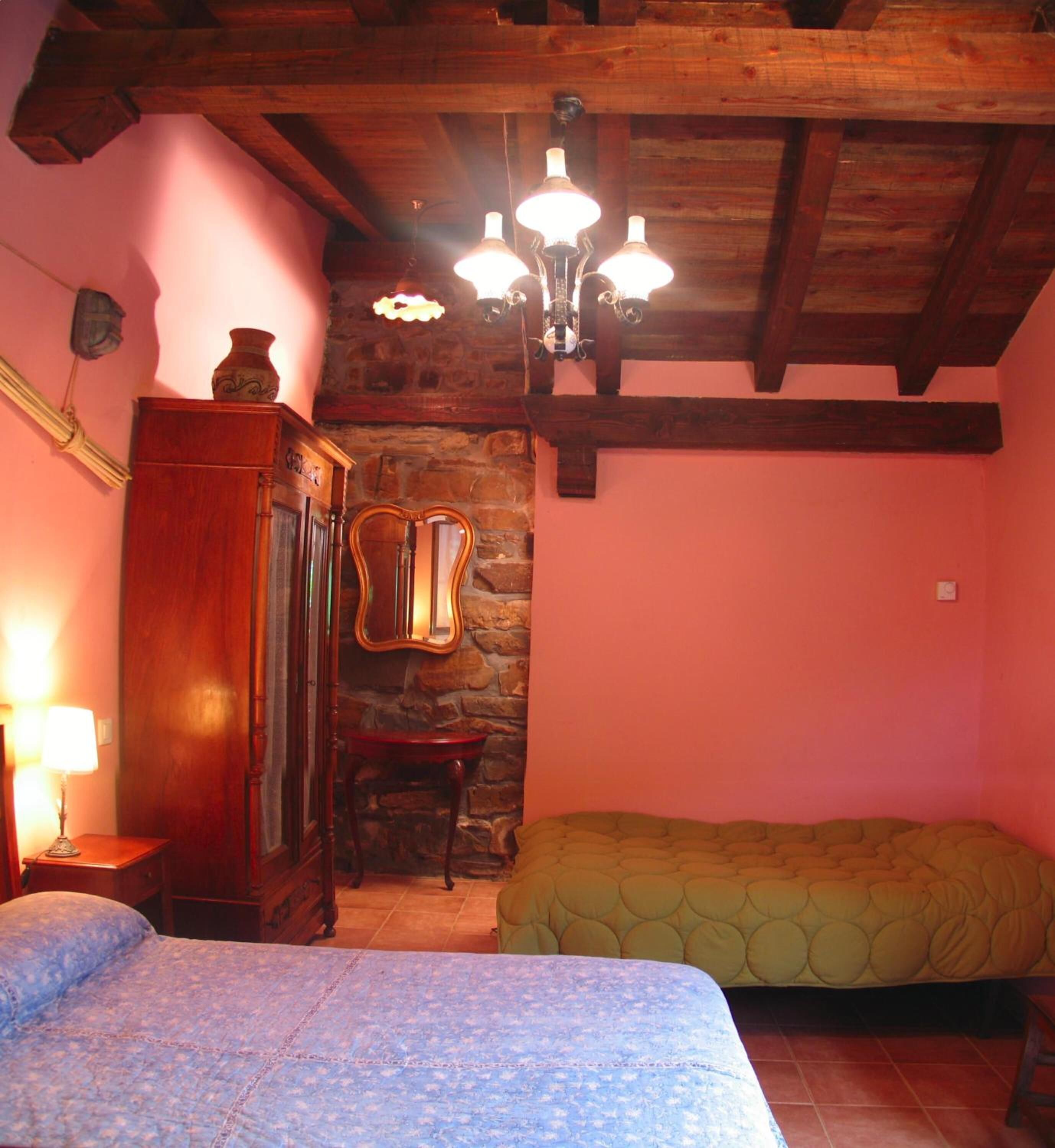 Une chambre avec un plafond en bois, un mur en pierre, un lit, une chaise et une commode.