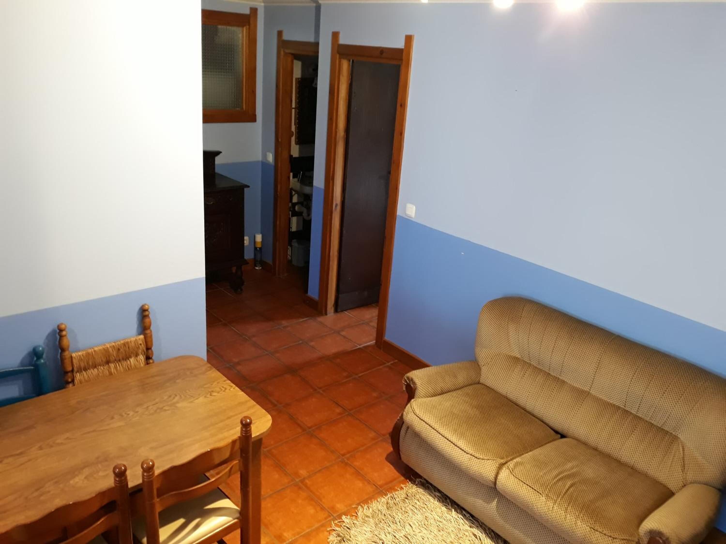Un soggiorno con tavolo da pranzo in legno, sedie, un divano e pavimento piastrellato.