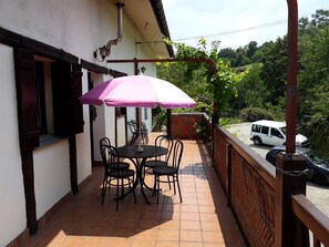 A patio with a table and chairs under a pink umbrella, a white van parked nearby, and a view of greenery in the background.