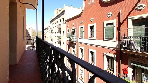 A narrow balcony with a metal railing overlooking a row of buildings with red and white facades, some with balconies and shutters. - CLASSBEDROOM BARCELONA BEACH 5 APARTMENT (Barcelona)
