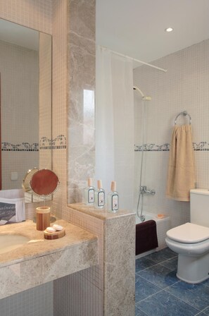 Une salle de bain avec un meuble-lavabo en marbre, un miroir rond, une douche et des toilettes.