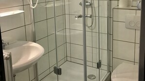 Un baño moderno con ducha de vidrio, lavamanos blanco y retrete.