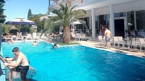 A hotel pool area with a clear blue pool, lounge chairs, and a multi-story building with balconies. - Hotel Philippos (Livadia)