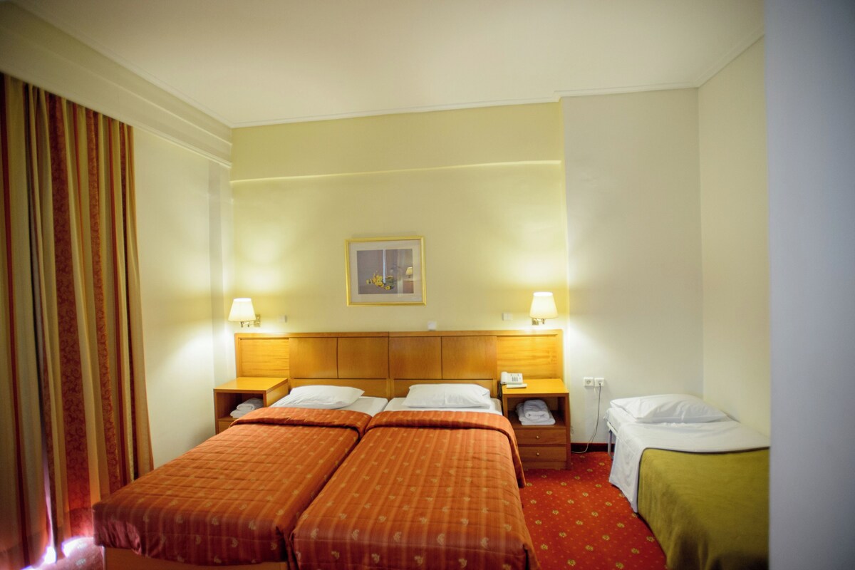 A hotel room with two beds, a nightstand with a lamp, a telephone, and a framed picture on the wall.