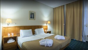 A hotel room with a large bed, two bedside tables, lamps, a painting on the wall, and a window with curtains. - Hotel Philippos (Livadia)