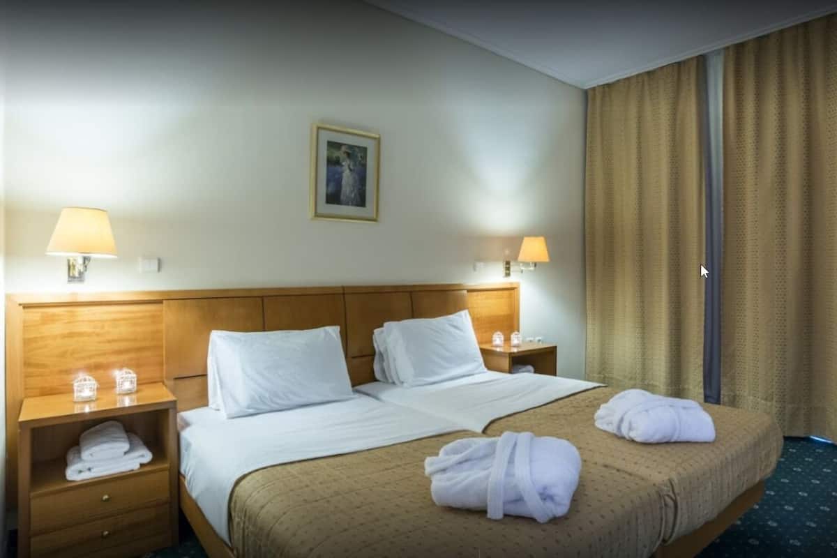 A hotel room with a large bed, two bedside tables, lamps, a painting on the wall, and a window with curtains.