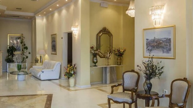 A spacious lobby with a marble floor, a white sofa, two wooden chairs, a table, a mirror, and a chandelier. - Hotel Philippos (Livadia)