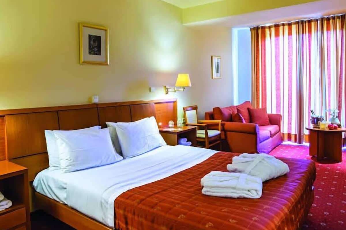 A hotel room with a large bed, a desk, a chair, a sofa, and a window with curtains.