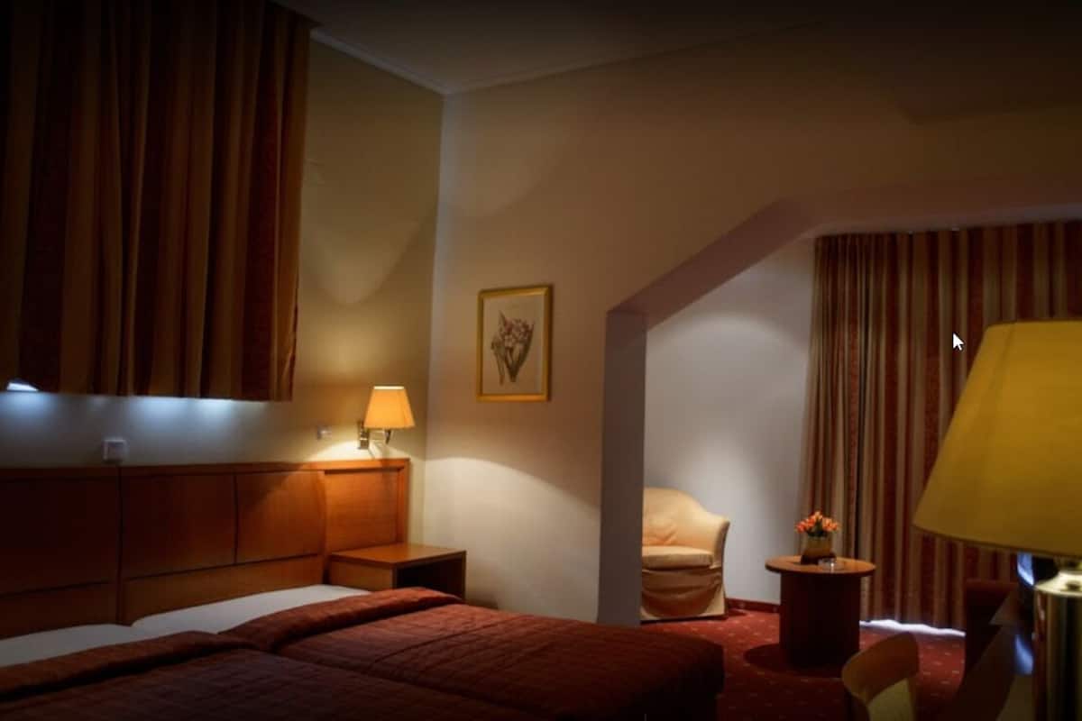 A hotel room with a bed, a chair, a desk, and a lamp.
