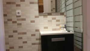 Un bagno con pavimento piastrellato, un water, un lavandino con uno specchio sopra e una cabina doccia in vetro.