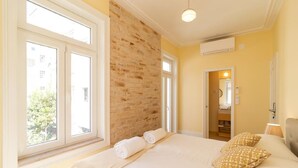 A bedroom with a large bed, a brick accent wall, and a view of the outside. - GuestHouse - Deluxe Double Room with Balcony (Room 8 Seraphim ) (Lisboa)