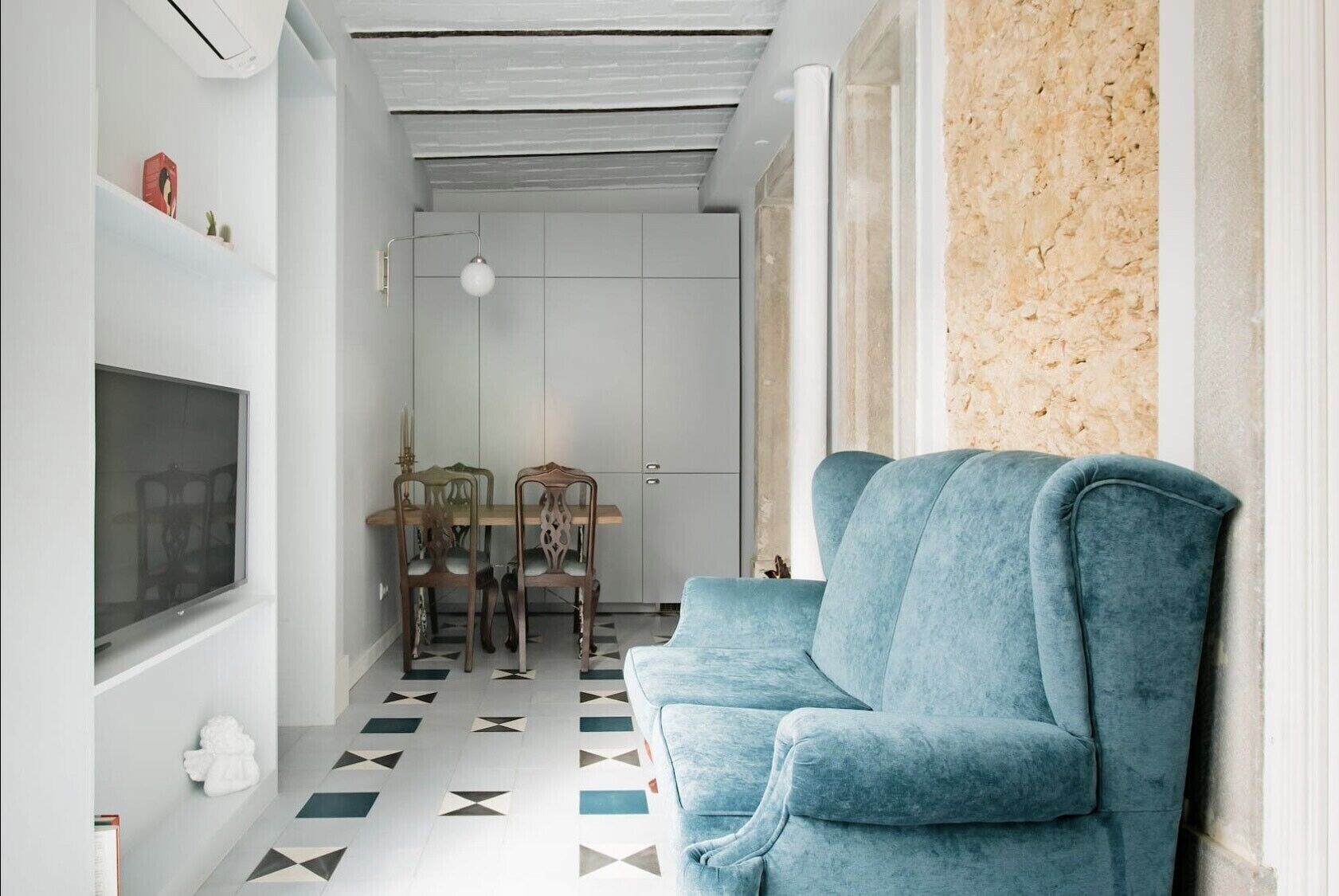 A modern living room with a blue sofa, a dining table with chairs, and a TV on the wall.
