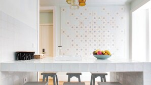 A modern kitchen with white tiles, a fruit bowl, and a remote control on the counter. - GuestHouse - Deluxe Double Room with Balcony (Room 8 Seraphim ) (Lisboa)