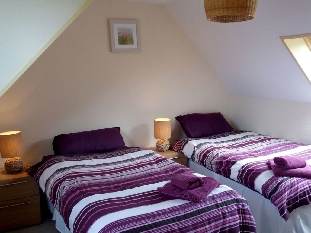 A bedroom with two beds, each with purple bedding and a lamp on the nightstand.