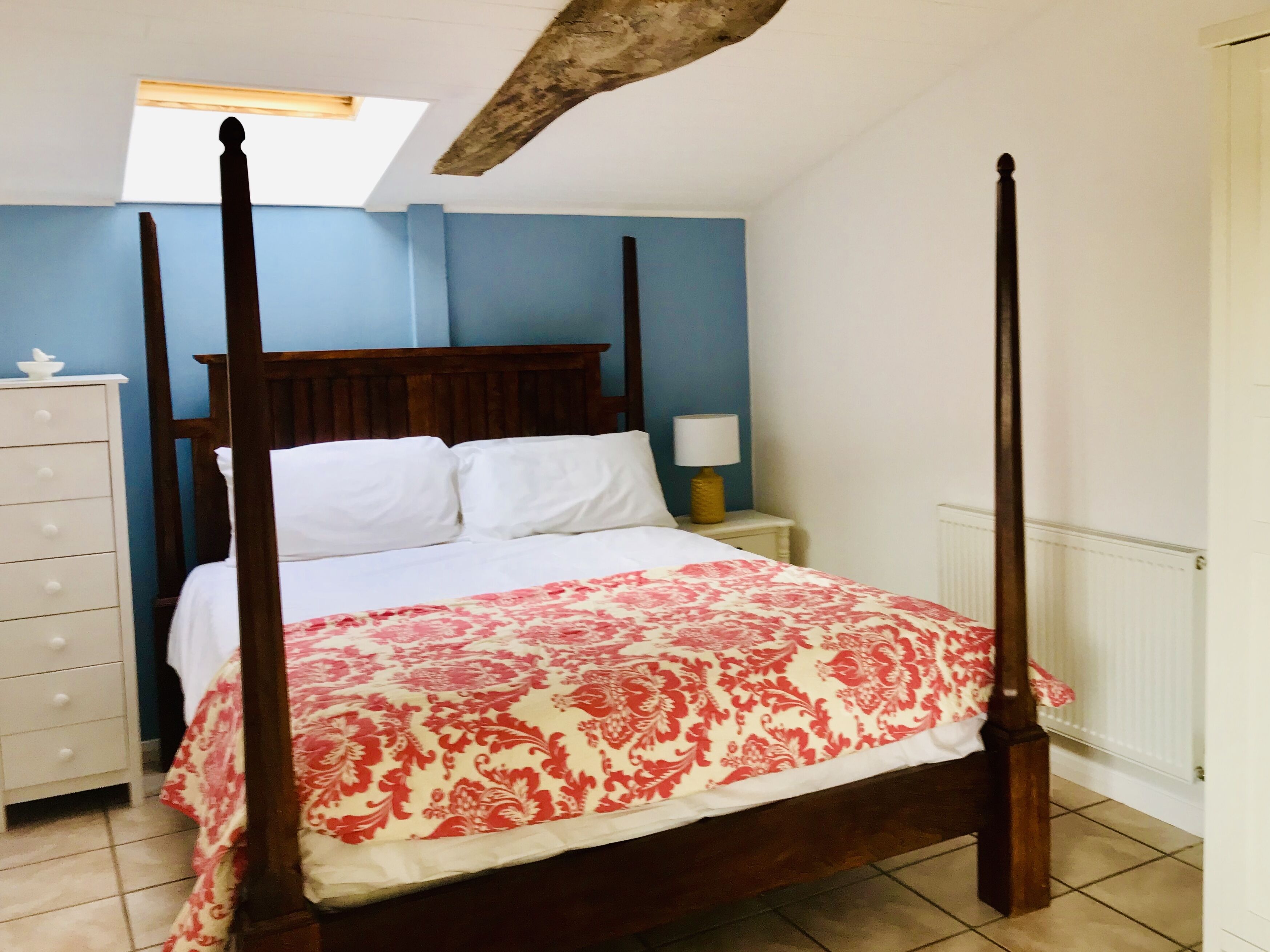 A four-poster bed with a floral bedspread, a nightstand with a lamp, and a dresser with drawers.