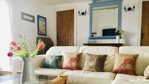 Een woonkamer met een witte bank, een glazen salontafel en een vaas met bloemen.
