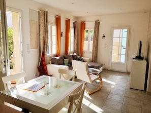 Relax in this open-plan living and dining area featuring a glass-top dining table, sofa, and TV on a stand.
