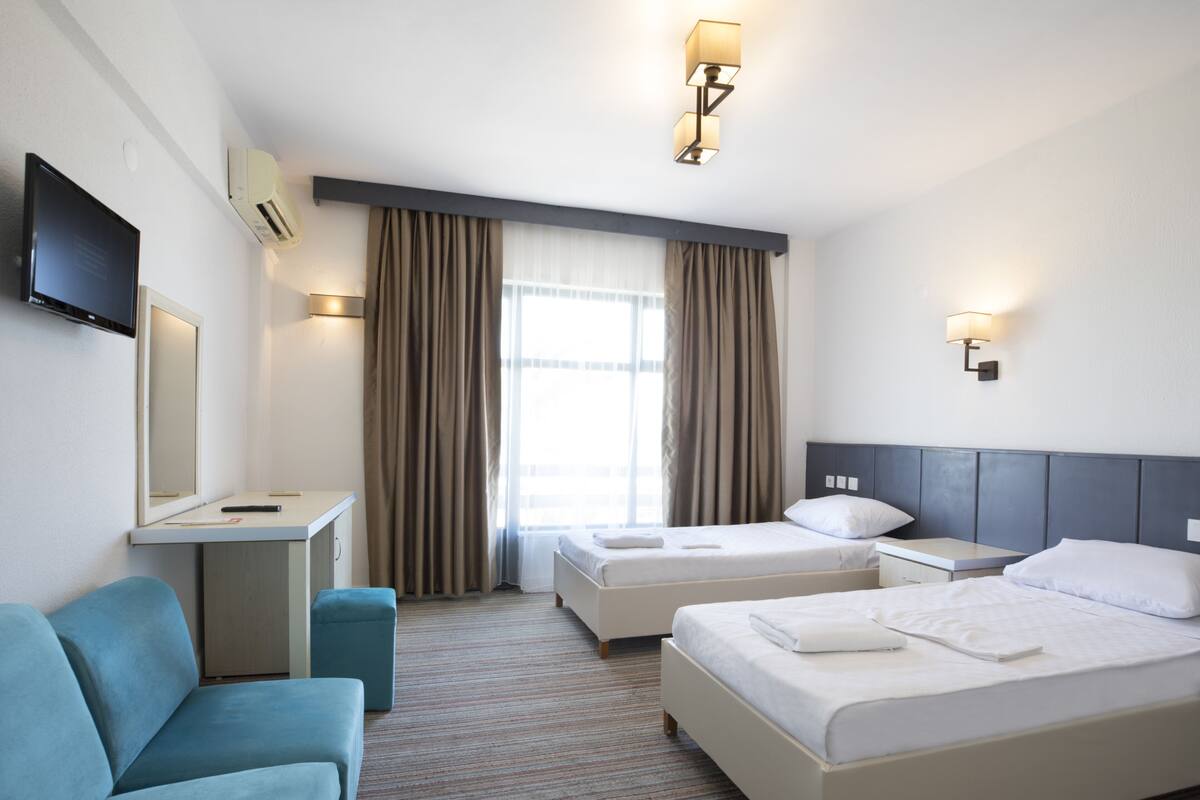 Une chambre d’hôtel avec deux lits, un bureau, une chaise, une télévision et une fenêtre avec des rideaux.