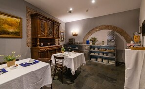 Un coin repas avec une table dressée pour deux personnes, un buffet en bois orné de sculptures complexes et une arche en pierre.