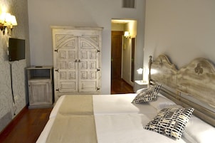 A bedroom with a bed, two pillows, a nightstand, a wardrobe, and a television.