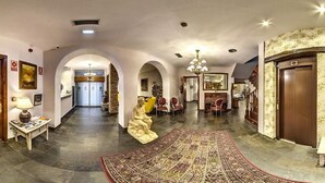 Un pasillo amplio con un tapete grande y decorativo, puertas de madera y un candelabro.