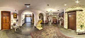 A spacious hallway with a large, ornate rug, wooden doors, and a chandelier. - Alda Vía León (León)