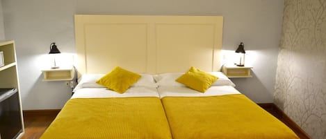 A double bed with two yellow pillows, a white headboard, and two bedside lamps.
