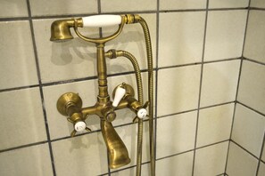 Un accessorio da bagno in ottone con due manopole e un tubo flessibile, fissato a una parete rivestita di piastrelle.