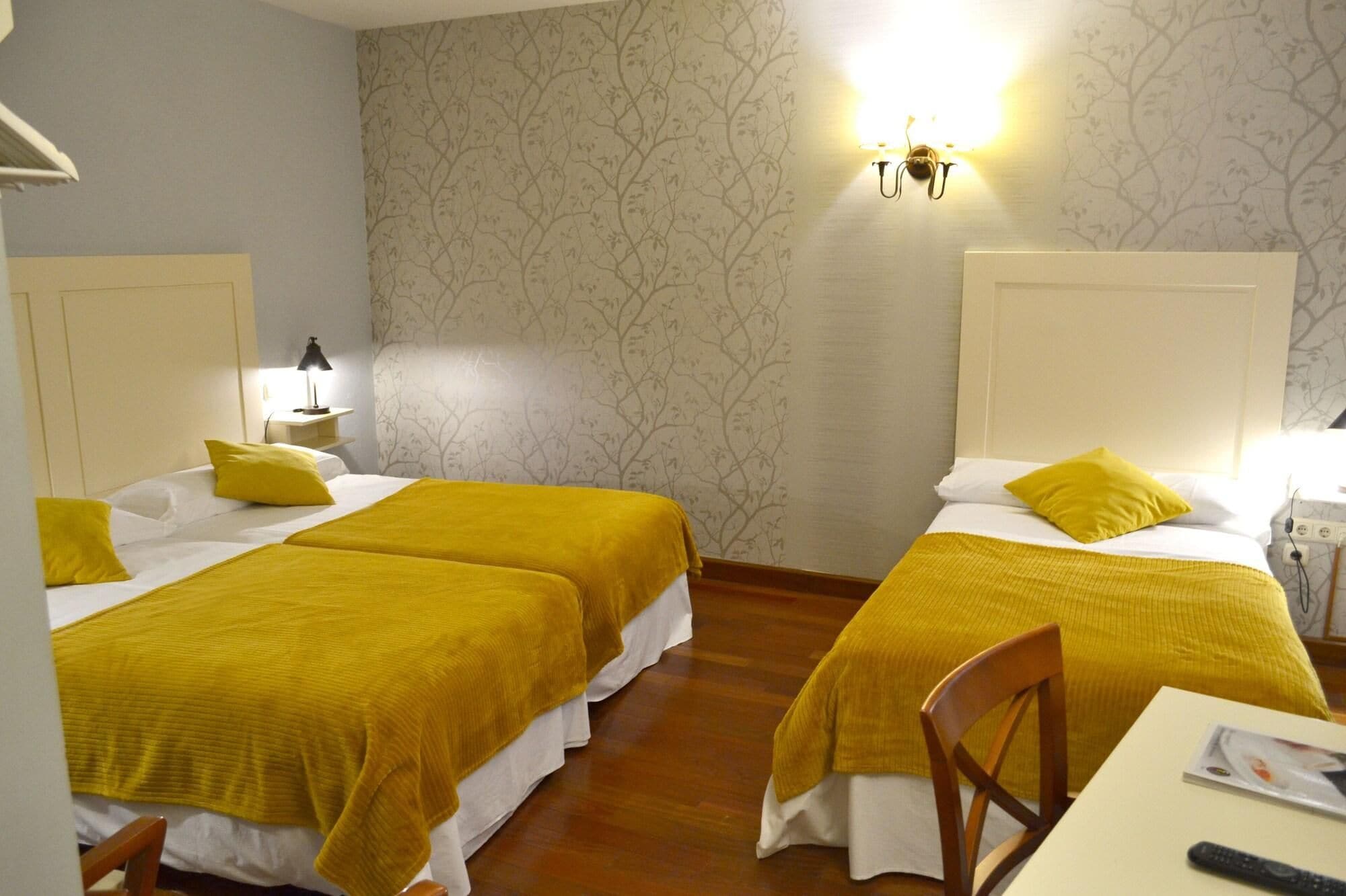 Ein Hotelzimmer mit zwei Betten, jeweils mit einer gelben Bettdecke, einem Nachttisch mit Lampe und einer Wandleuchte.