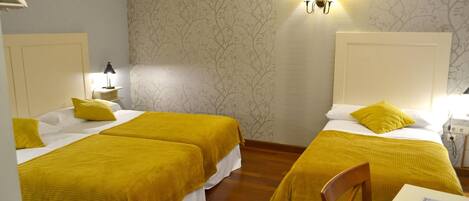 Ein Hotelzimmer mit zwei Betten, jeweils mit einer gelben Bettdecke, einem Nachttisch mit Lampe und einer Wandleuchte.