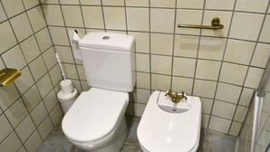Un baño con inodoro y bidé, paredes de azulejos y un asa metálica en la pared.