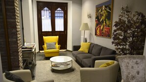 A living room with a yellow armchair, a grey sofa, a white armchair, a coffee table, and a painting on the wall. - Alda Vía León (León)