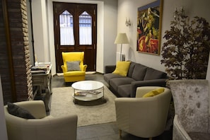 A living room with a yellow armchair, a grey sofa, a white armchair, a coffee table, and a painting on the wall. - Alda Vía León (León)