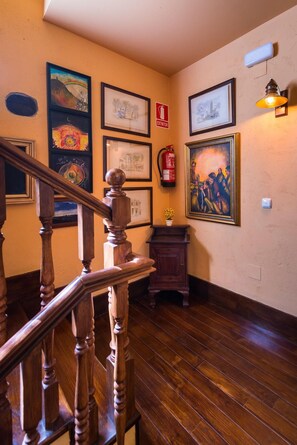 Un escalier en bois avec une rampe, un extincteur et des œuvres d’art encadrées accrochées aux murs.