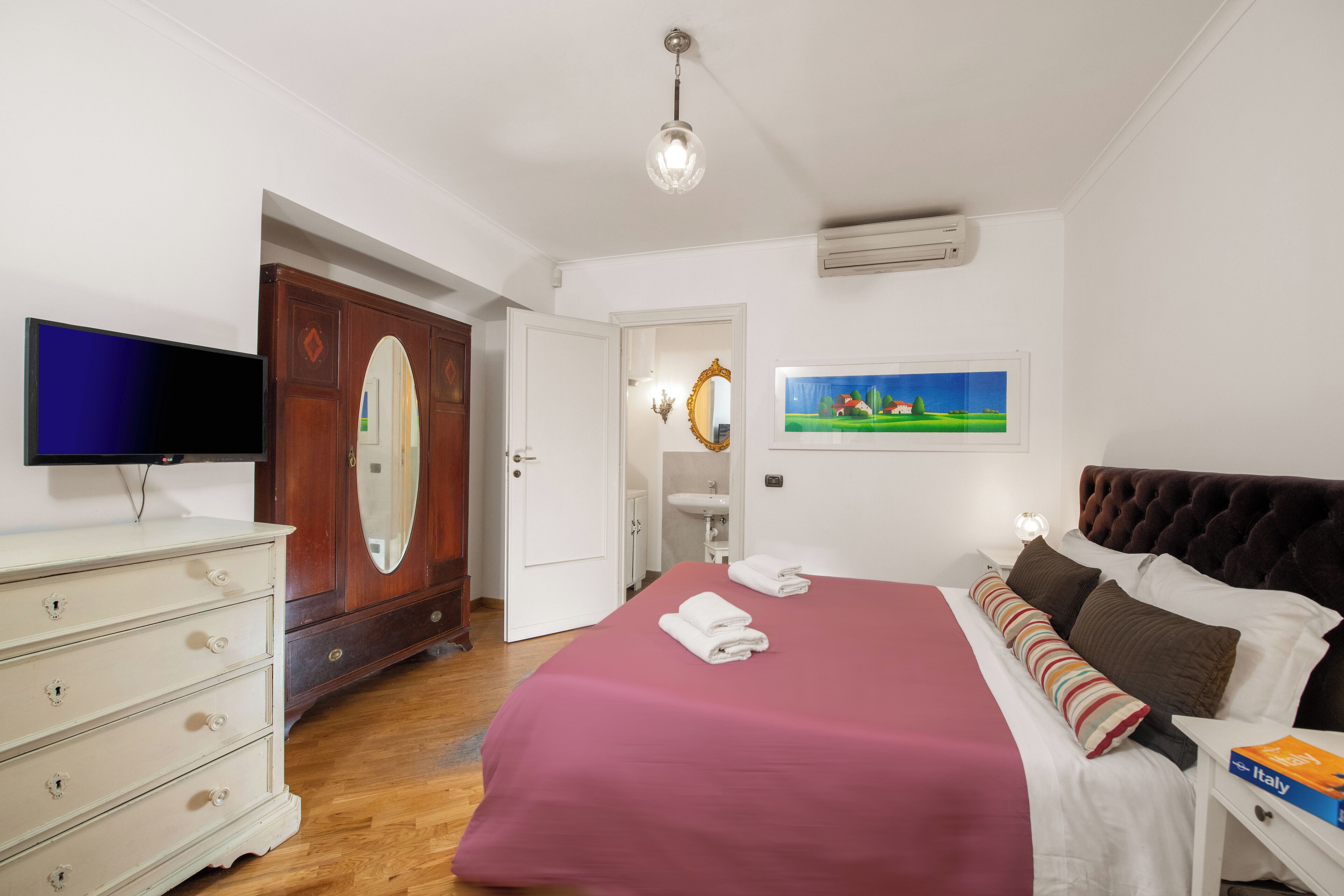 Un dormitorio con cama, cómoda, televisor, espejo y un cuadro en la pared.