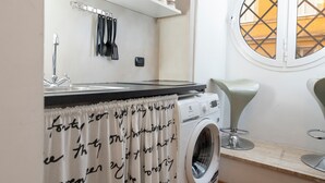 A compact laundry area with a washing machine, a sink, and a window with a view of buildings. - Corso Vittorio Apartments (Rome)