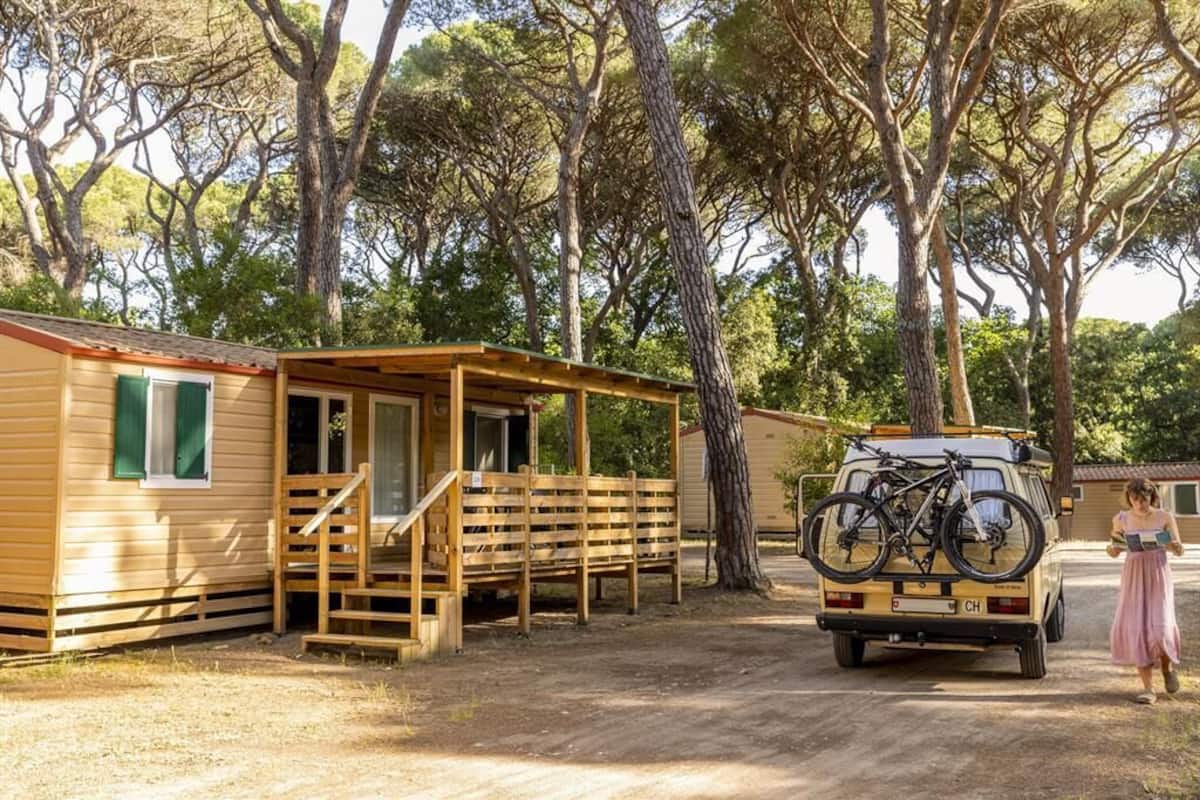 Eine Holzhütte mit Veranda, ein Fahrzeug mit Fahrradträger und eine Person, die geht.