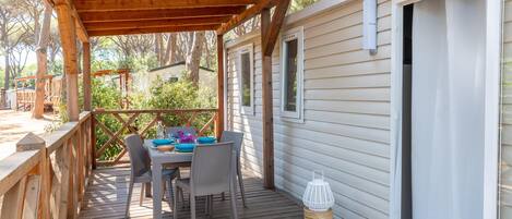 A wooden deck with a table and chairs, a covered area, and a white building with windows.