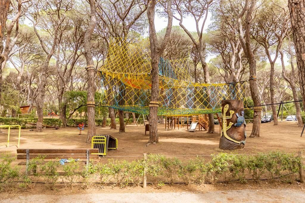 A playground with climbing structures and swings surrounded by trees.