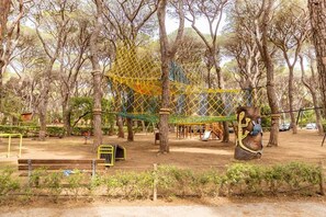 A playground with climbing structures and swings surrounded by trees. - Gitavillage Le Marze (Grosseto)
