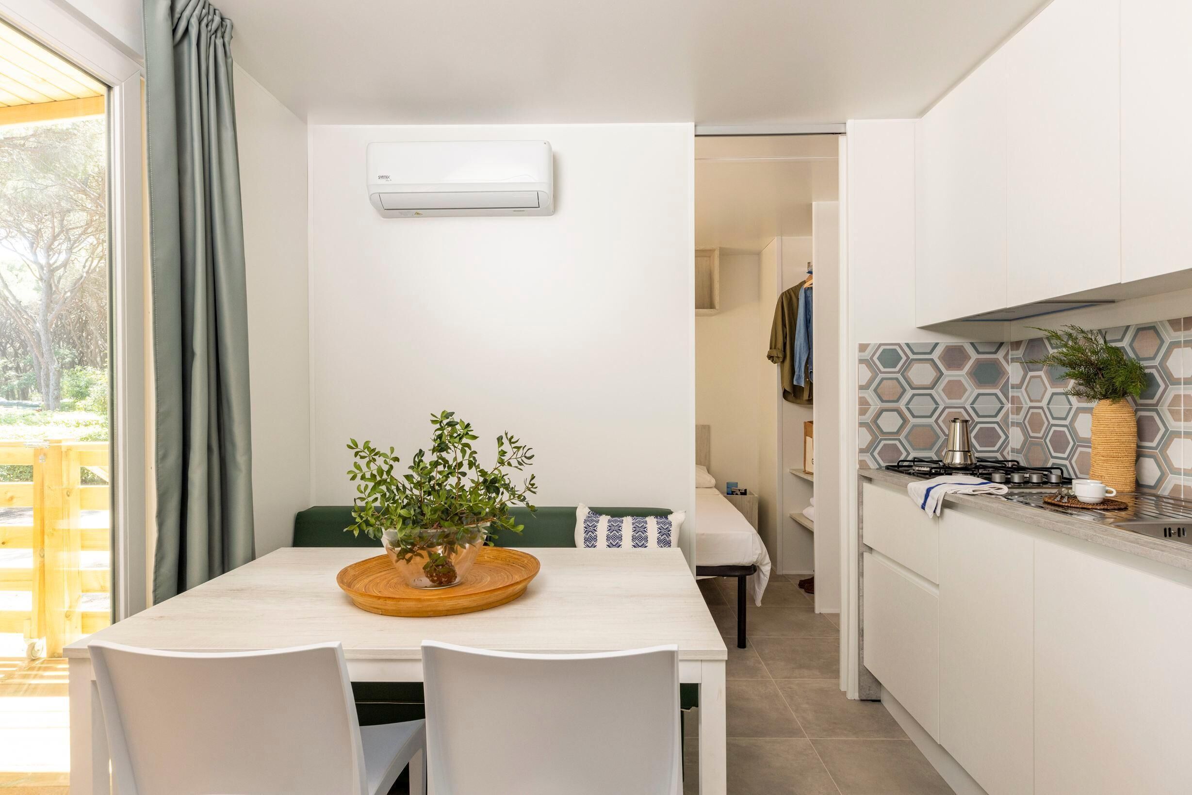Une cuisine moderne avec des meubles blancs, une table à manger en bois et une plante en pot.