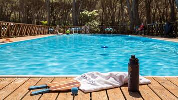Une terrasse en bois avec une piscine, une serviette et une bouteille d’eau.