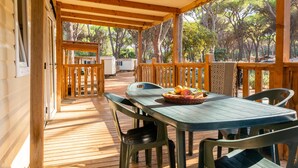 A wooden deck with a table and chairs, a basket of fruit, and a view of trees and a building in the background. - Gitavillage Le Marze (Grosseto)