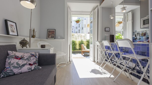 Een moderne woonkamer met een grijze bank, een witte salontafel en een eetgedeelte met witte stoelen en een blauwe betegelde achterwand.