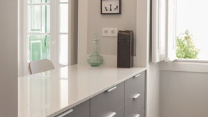 Een moderne keuken met een wit aanrecht, grijze kastjes, hanglampen en een raam met uitzicht op groen.