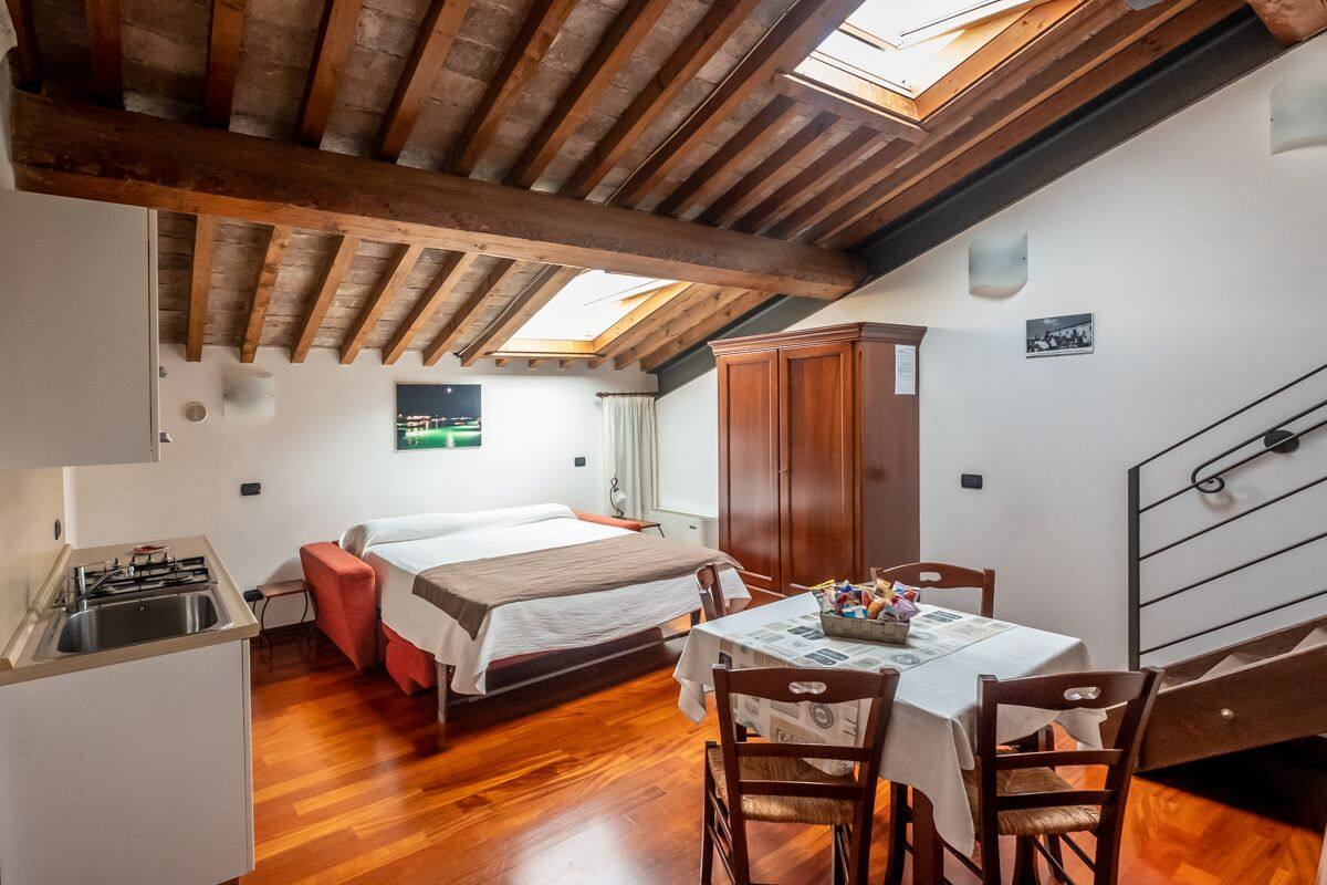 A compact room with a bed, a dining table with chairs, a wooden cabinet, and a skylight.