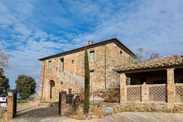 A stone building with a staircase leading to the entrance, a small garden area, and a metal gate.