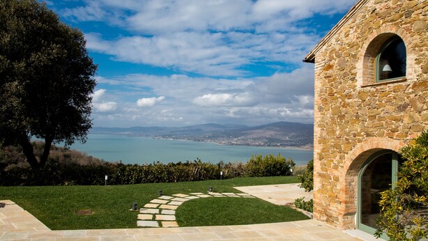 A stone building with a view of a body of water and mountains in the distance. - Villa Torricella (Magione)