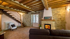 A cozy living room with a stone fireplace, a staircase, and a sofa. - Casale Pietrenta (Cortona)