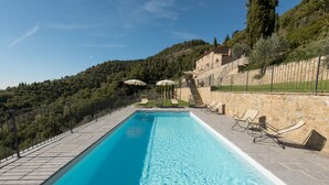 A rectangular swimming pool with clear blue water, surrounded by stone steps and a stone wall. There are lounge chairs and umbrellas along the poolside. - Casale Pietrenta (Cortona)